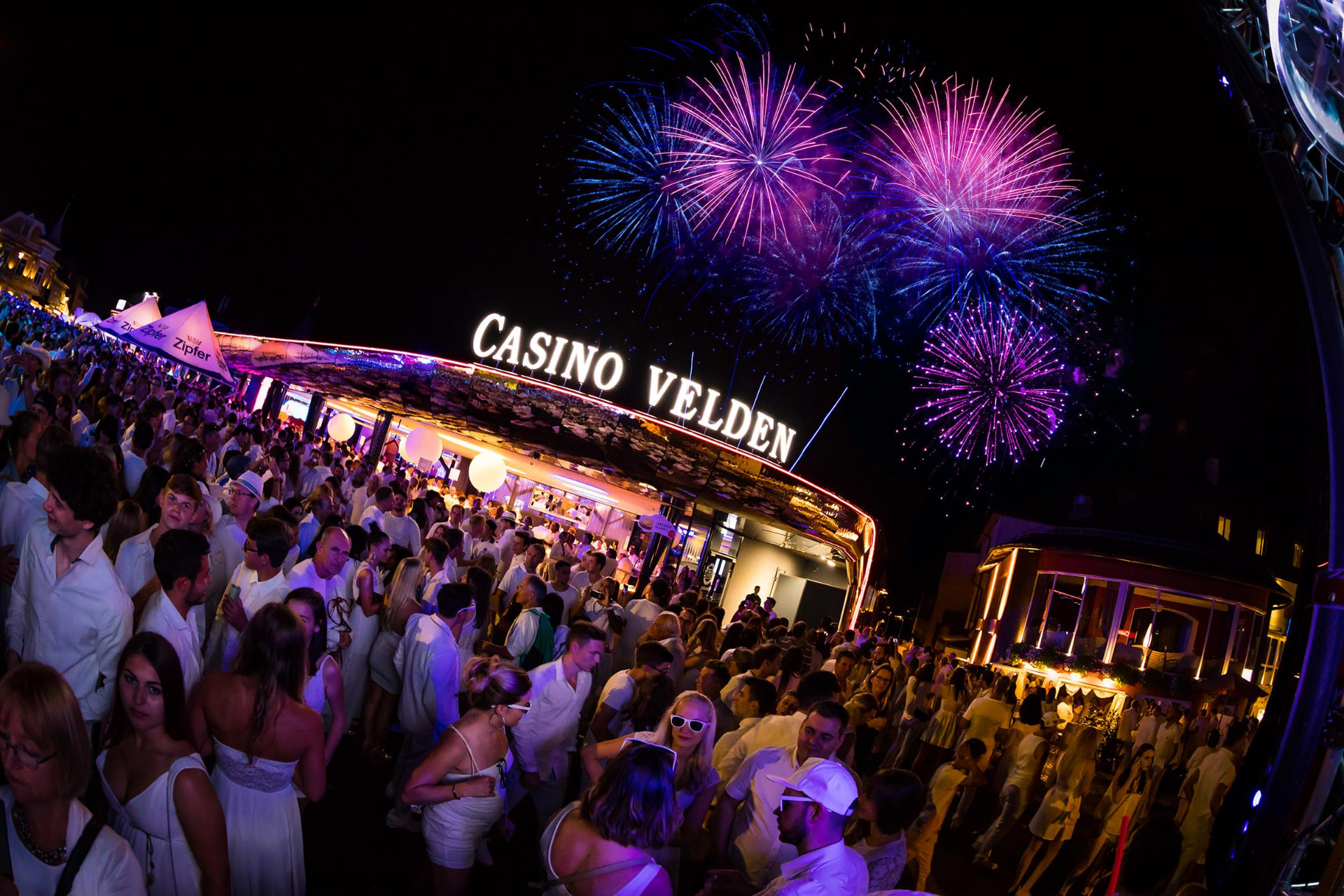 Feiernde in Weiß mit Feuerwerk vor dem Casino Velden